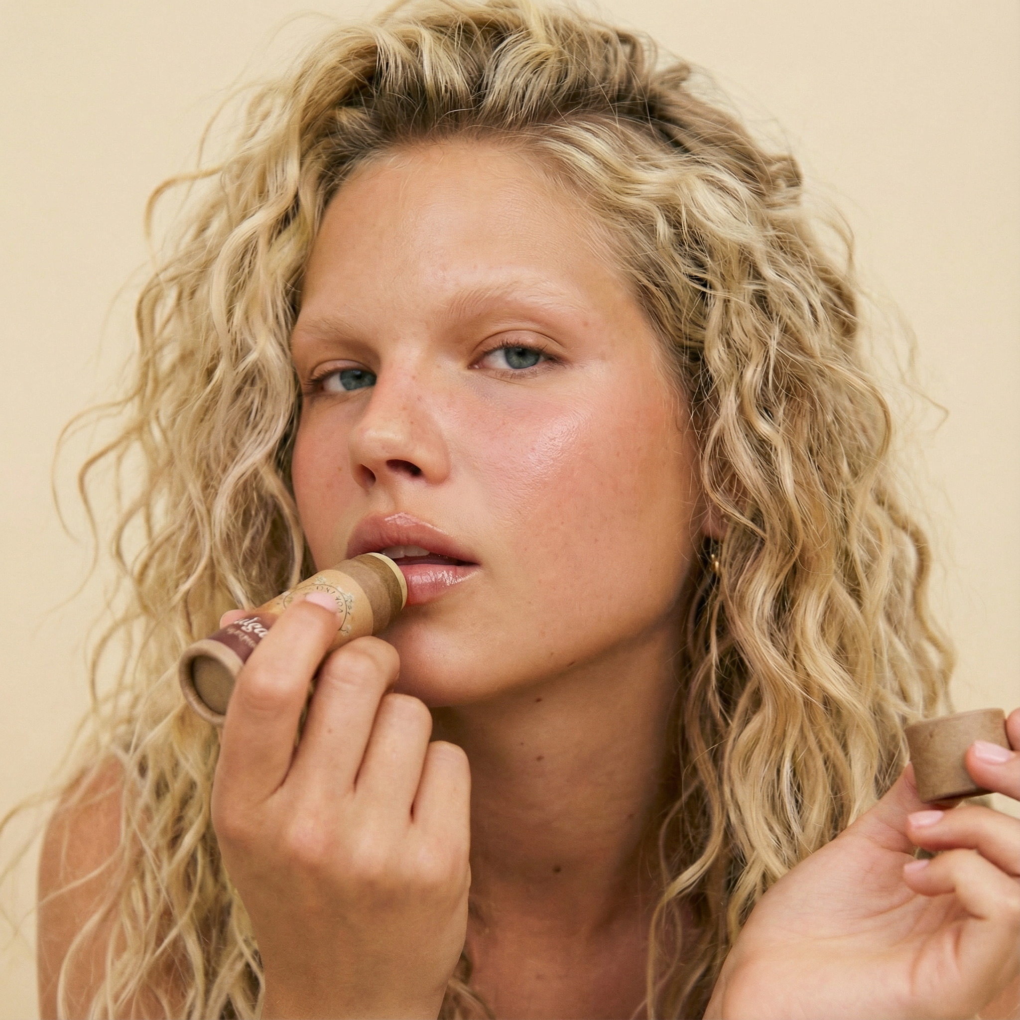 Person applying Talga Kiss tallow lip balm, holding the cap in their other hand.