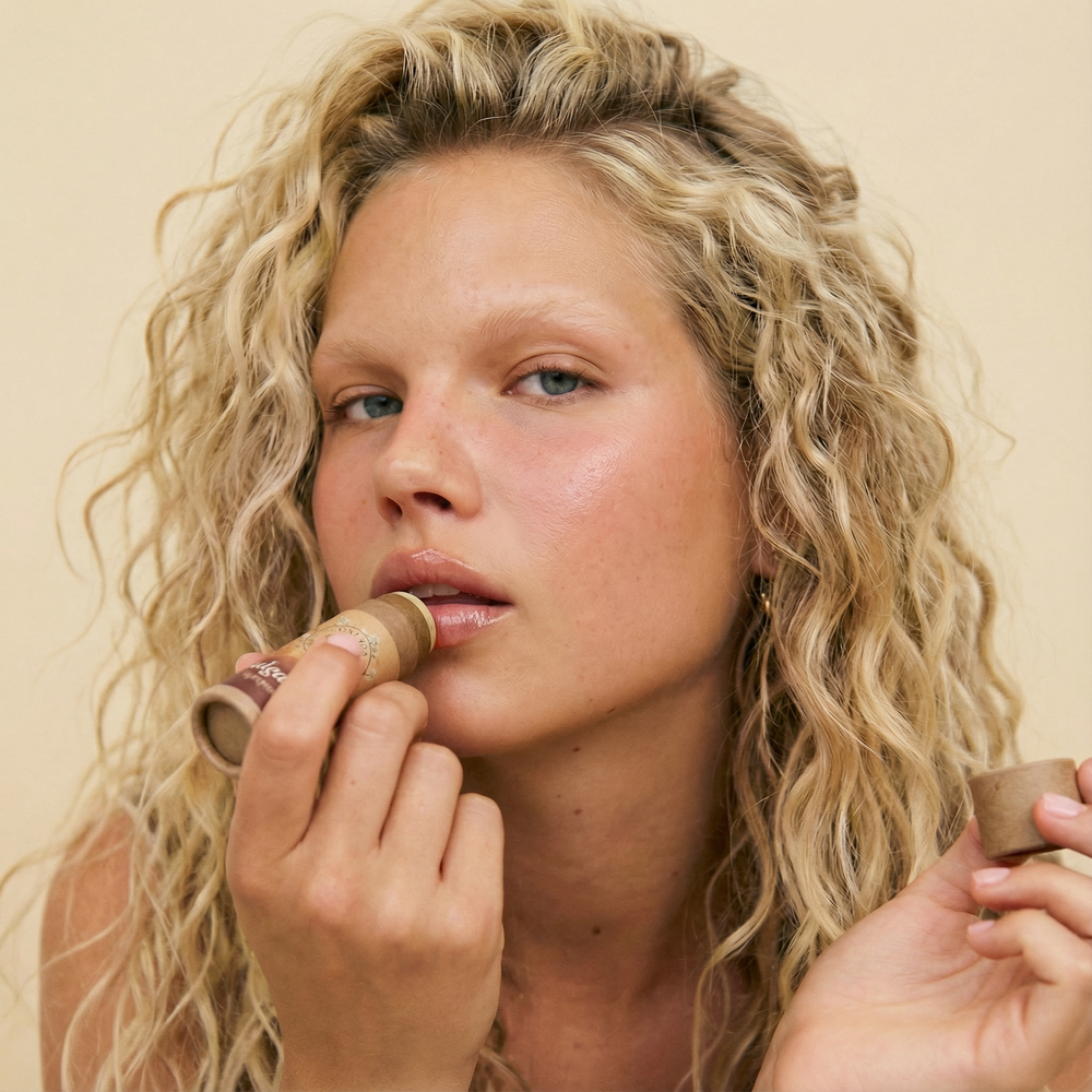 Talga Kiss leppepomade lip balm with the cap off and balm stick exposed on a beige background.